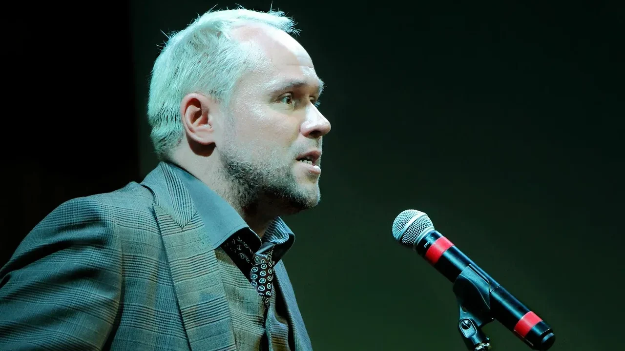 Prelegent na scenie konferencyjnej z mikrofonem przed publicznością — prezentacje publiczne jako umiejętność techniczna